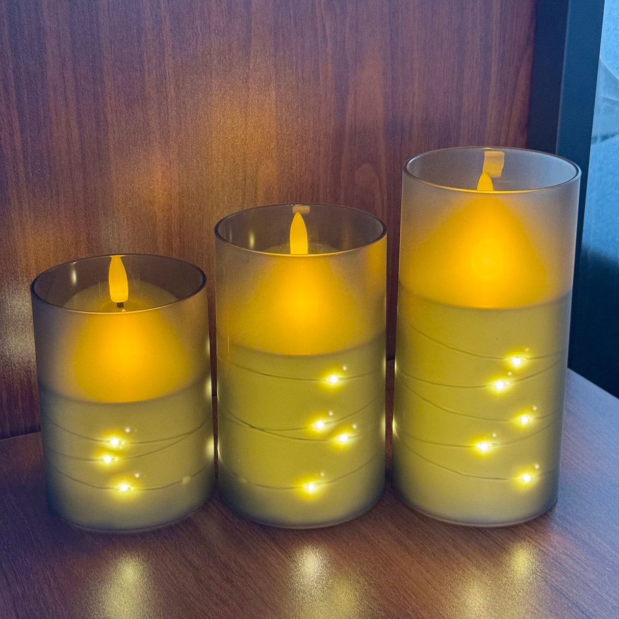 Three illuminated candles in glass holders on a wooden surface.